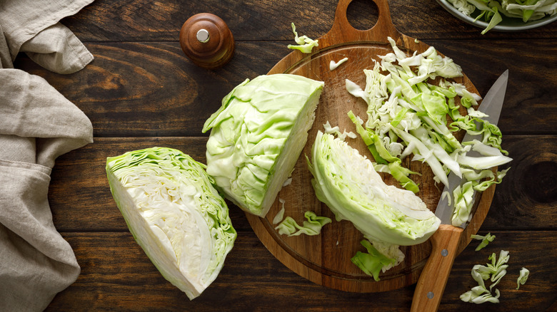 Halved and shredded cabbage is styled on a cutting board and wooden table.