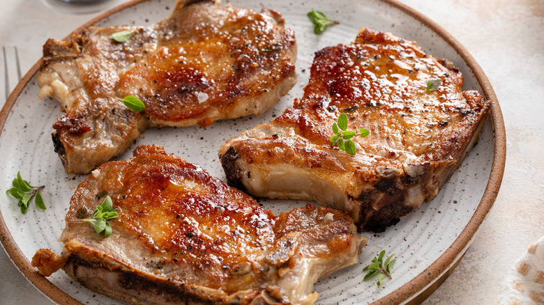 Three pieces of perfectly seared pork chops on bone on a grey platter.
