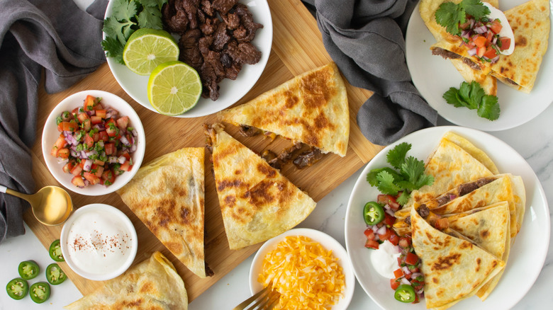 quesadillas on a wooden board and two white plates