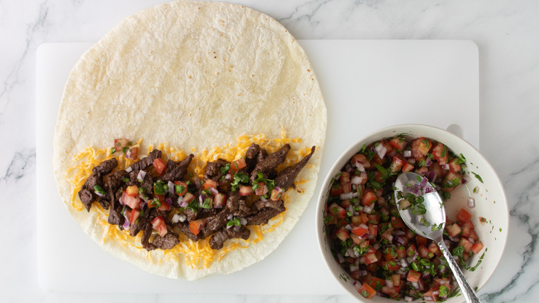 flour tortilla partially covered with meat, salsa, and shredded cheese