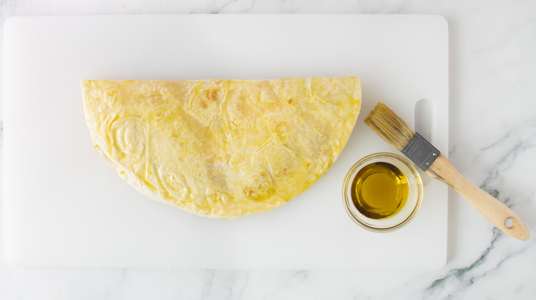 folded flour tortilla on a white plastic board with oil and a paintbrush