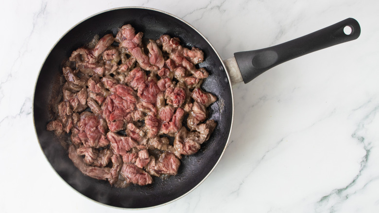partially cooked steak strips in a black frying pan