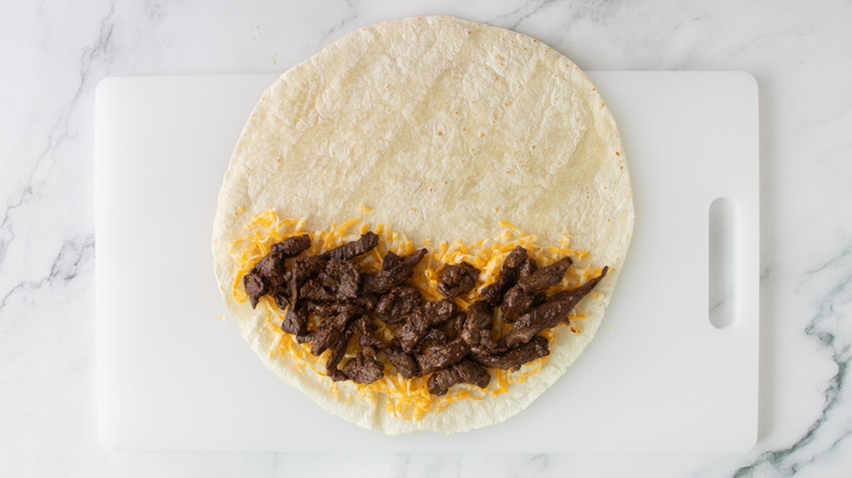 flour tortilla partially covered with meat and shredded cheese