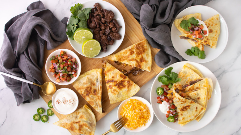quesadillas on a wooden board and two white plates