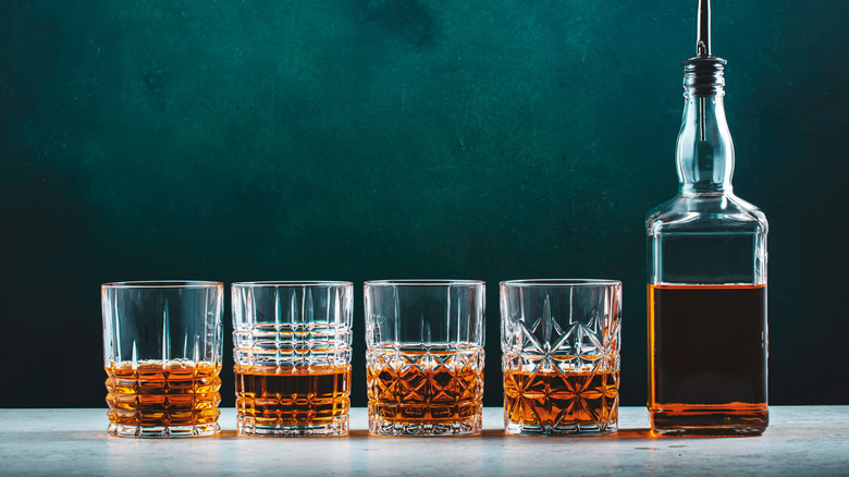 A row of glasses of Scotch beside a single bottle.