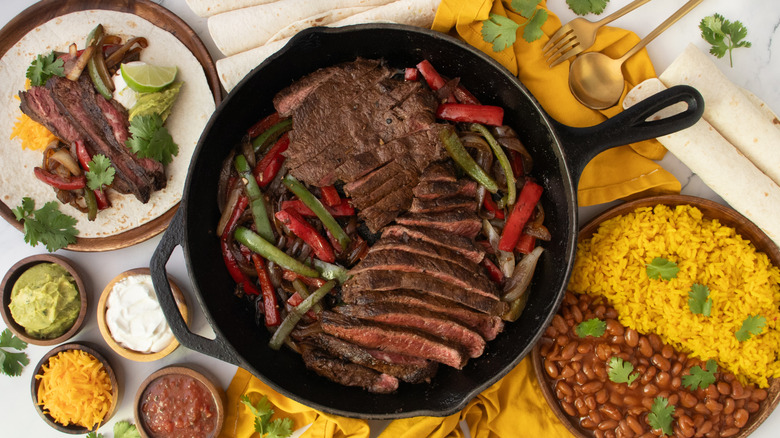 Overhead shot of steak fajitas, condiments, flour tortillas, and sides.