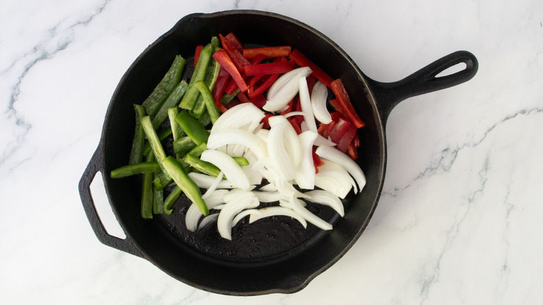 Raw onion and green and red bell peppers in a large cast iron skillet