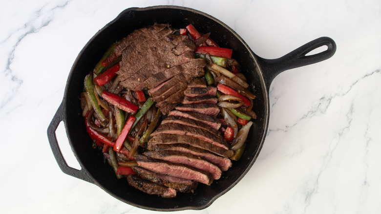 Sliced steak, peppers, and onions in a large cast iron skillet