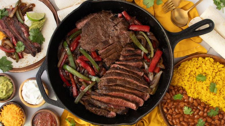 Overhead shot of steak fajitas, condiments, flour tortillas, and sides.