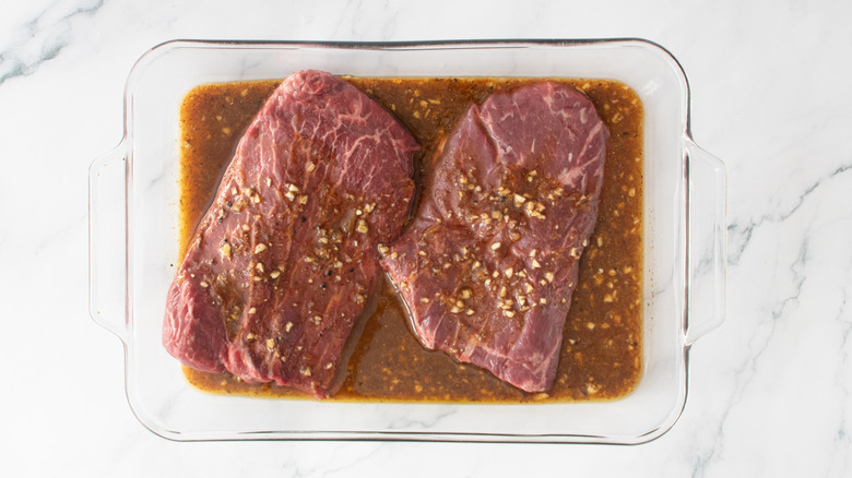 Two skirt steaks in a glass casserole dish covered in carne asada marinade