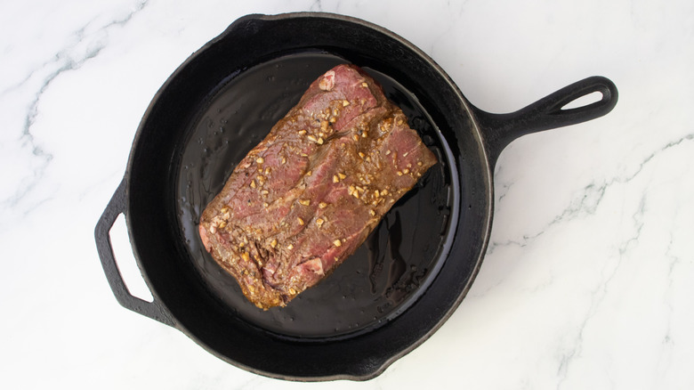 Raw, marinated skirt steak in a large cast iron skillet