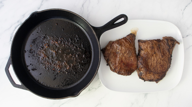 Seared steak removed from cast iron skillet and sitting on a large white plate