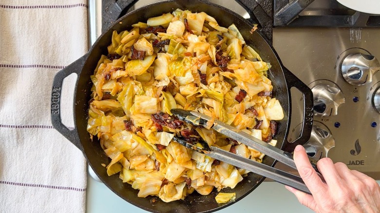 Adding crispy bacon bits to skillet cowboy cabbage with tongs
