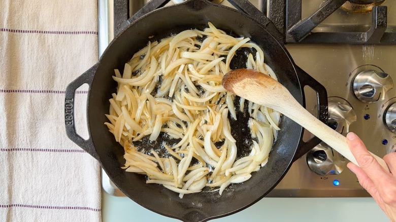 Sliced yellow onion in bacon fat in skillet on stovetop