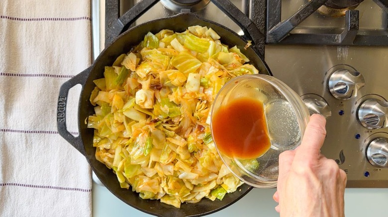 Pouring sauce into skillet cowboy cabbage on stovetop