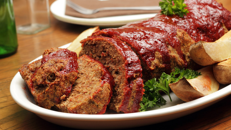 Glazed meatloaf has been sliced on a plate.