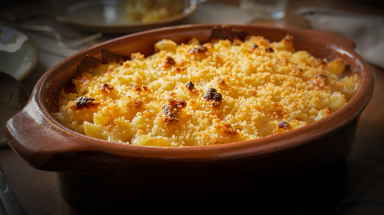 Baked macaroni and cheese topped with bread crumbs in a brown crock