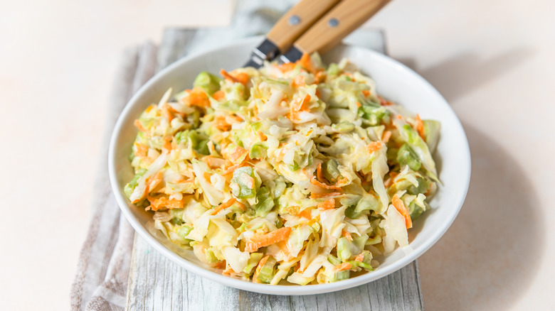 Coleslaw in a white bowl with serving spoons