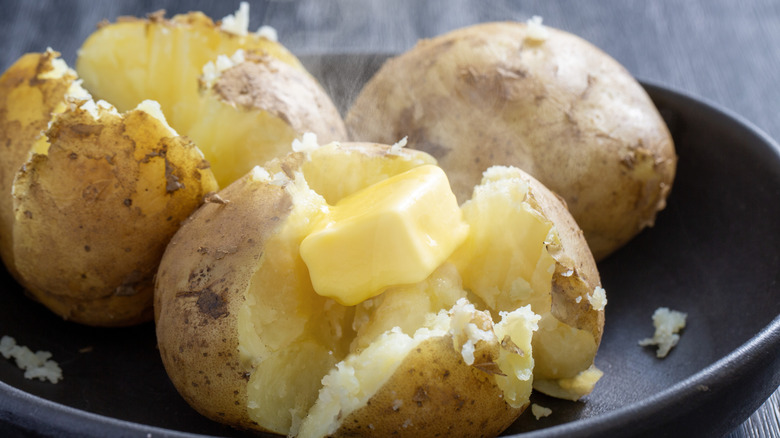 A bowl of three baked potatoes with butter.