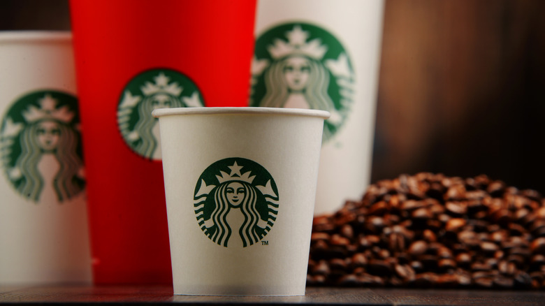 A short Starbucks coffee cup standing in front of a variety of other Starbucks cup sizes and a pile of coffee beans