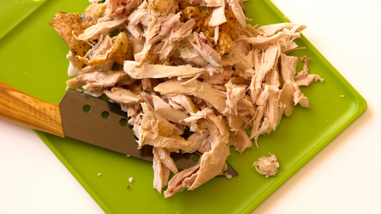 Shredded chicken on a green cutting board with a knife