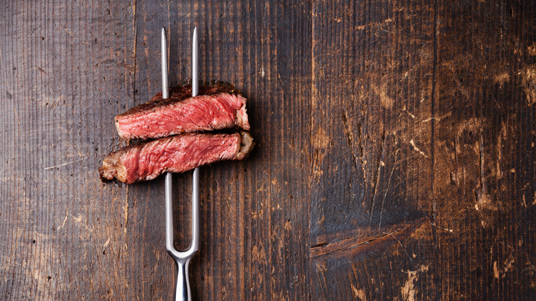 Slices of rosy steak are pierced on a two-pronged fork.