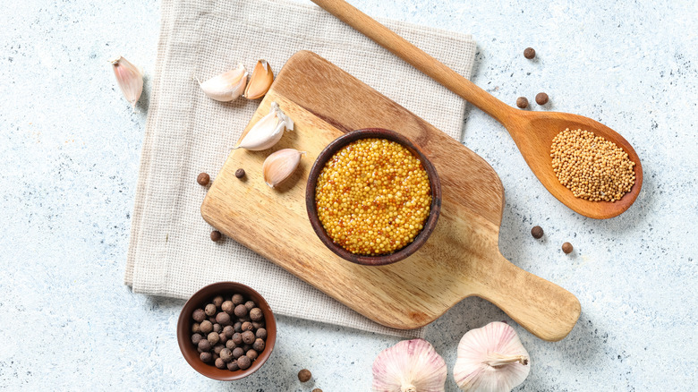 Whole grain dijon mustard, garlic, and peppercorns on a wooden cutting board.