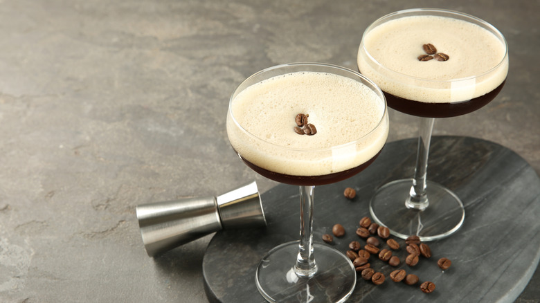 Two espresso martinis next to coffee beans on gray counter.