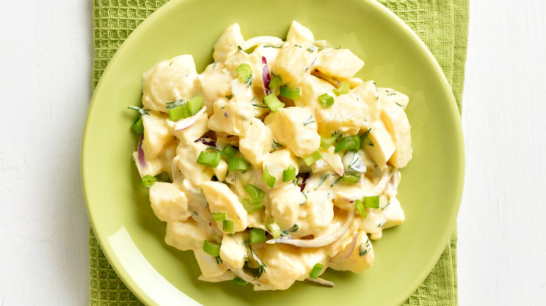 Homemade potato salad with egg, pickle, green onion with mayonnaise and yogurt dressing on green plate on white wooden background. Top view, flat lay