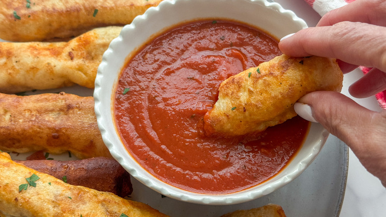hand dipping pizza mozzarella stick in marinara sauce