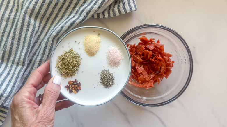 hand adding spices to bowl of chopped pepperoni
