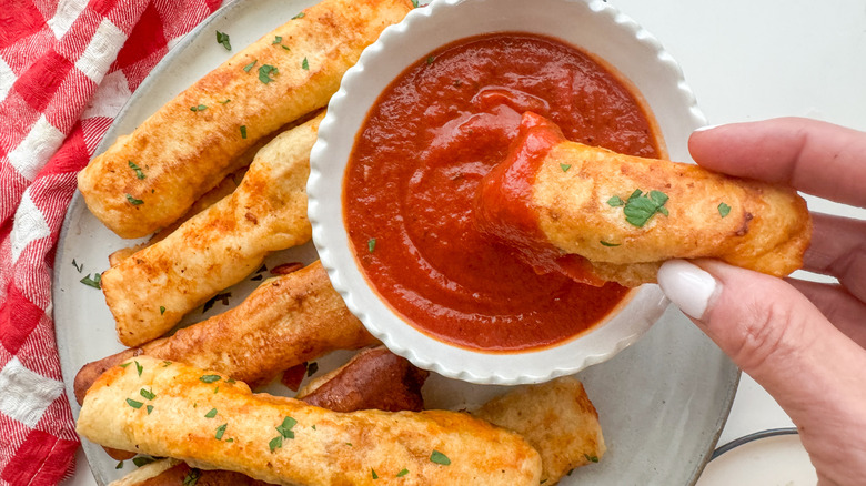 hand dipping pizza mozzarella stick in marinara sauce