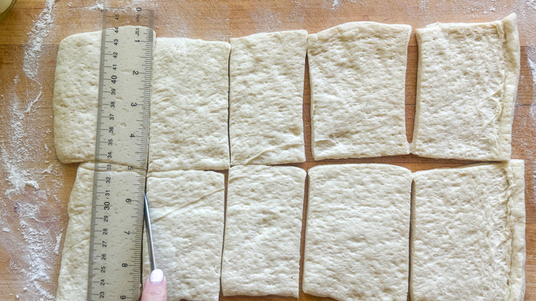 hand cutting pizza dough against ruler