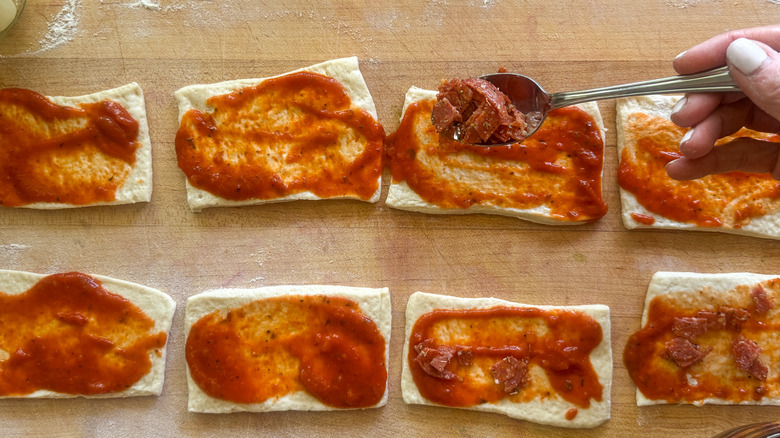 Spoon placing pepperoni onto sauced pizza rectangle
