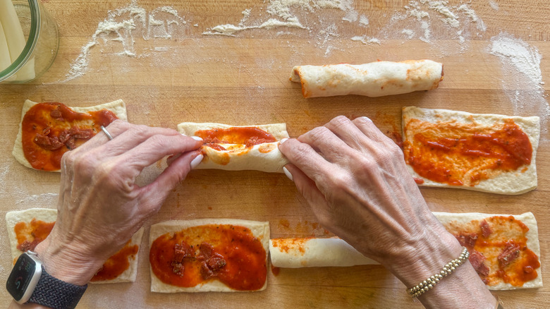 hands rolling up pizza dough rectangles