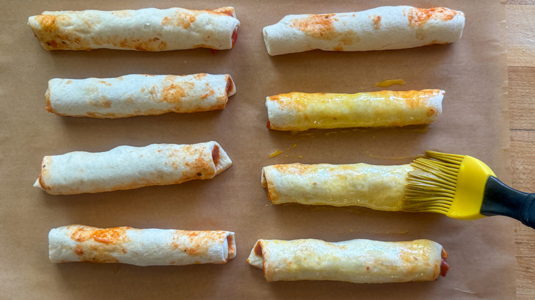 hand brushing rolled up pizza dough with egg