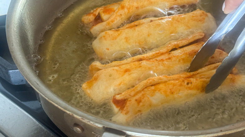 Pizza mozzarella sticks frying in oil with tongs
