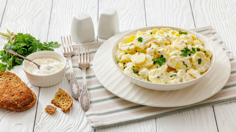 A bowl of potato salad topped with fresh garnish beautifully presented on a white table