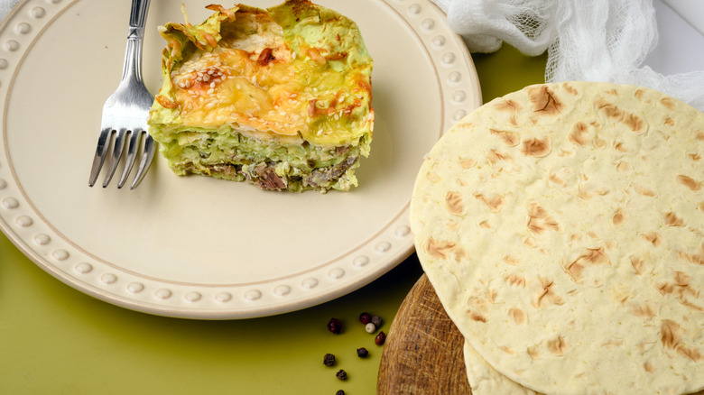 A slice of quiche on a plate next to lavash