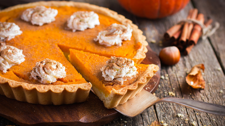 Pumpkin pie with whipped cream and cinnamon on a rustic background, top view.