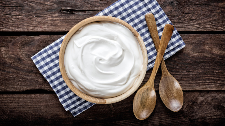 Sour cream in wooden bowl with wooden spoons and blue checkered napkin.