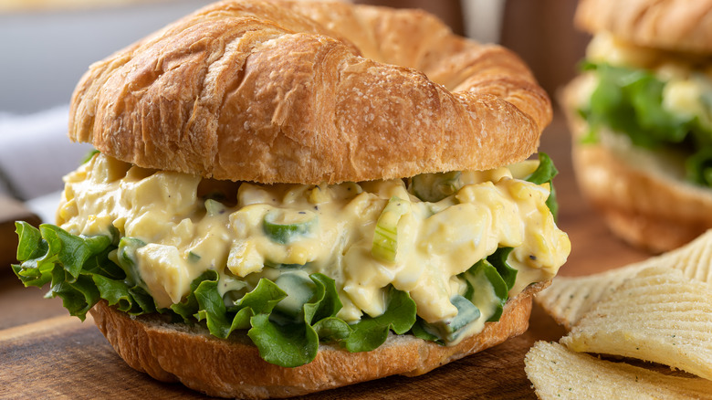 An egg salad sandwich with lettuce on a croissant.