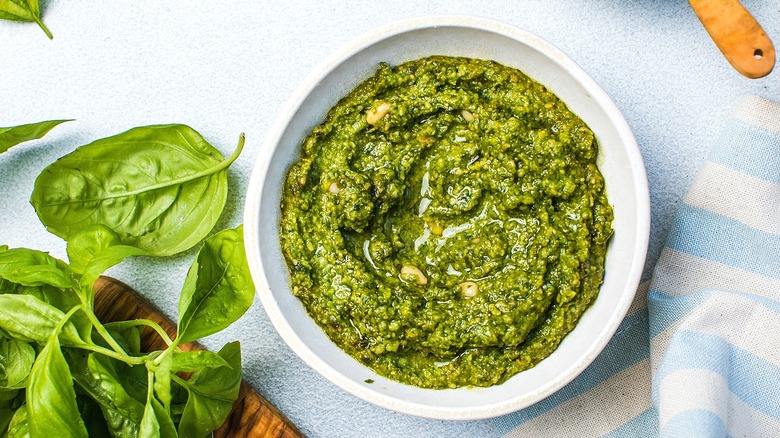 Pesto in a white bowl surrounded by fresh basil leaves