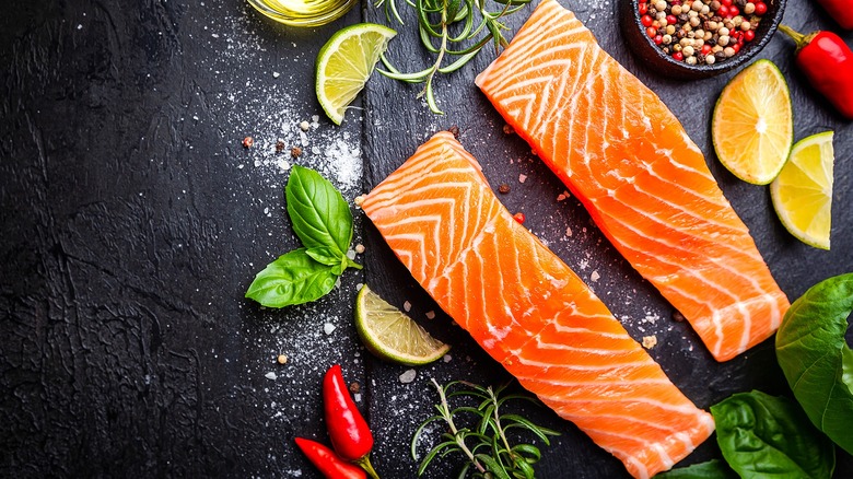 Raw salmon filets surrounded by fresh herbs, citrus, and peppercorns