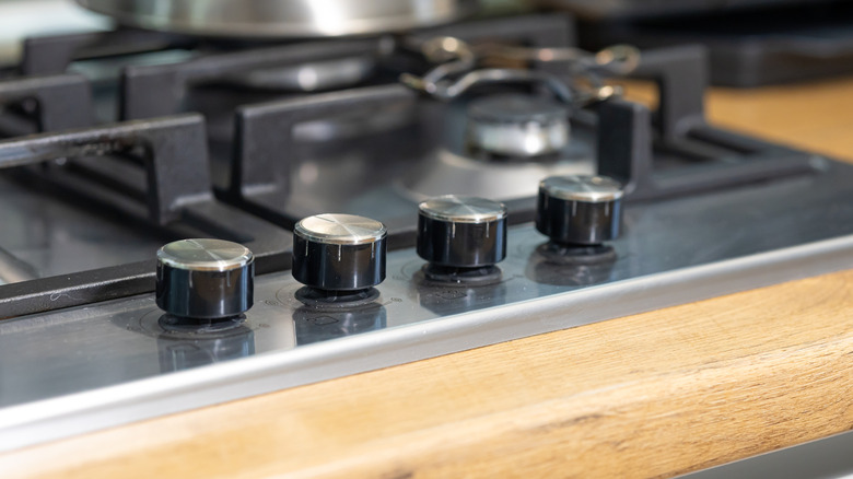 Close up of stovetop knobs on metal surface with wood counter beneath.