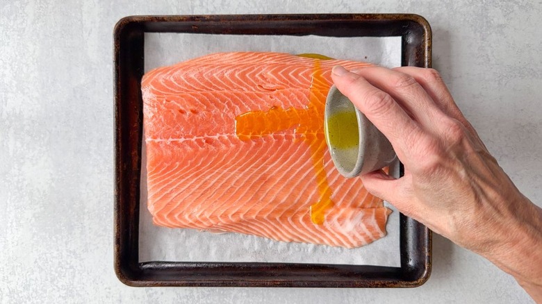 Drizzling olive oil over fresh salmon filet on parchment-lined baking sheet