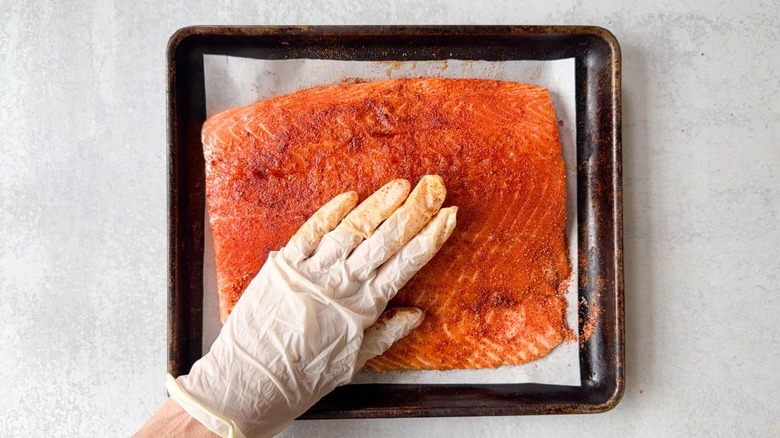 Rubbing seasoning into salmon filet using gloves
