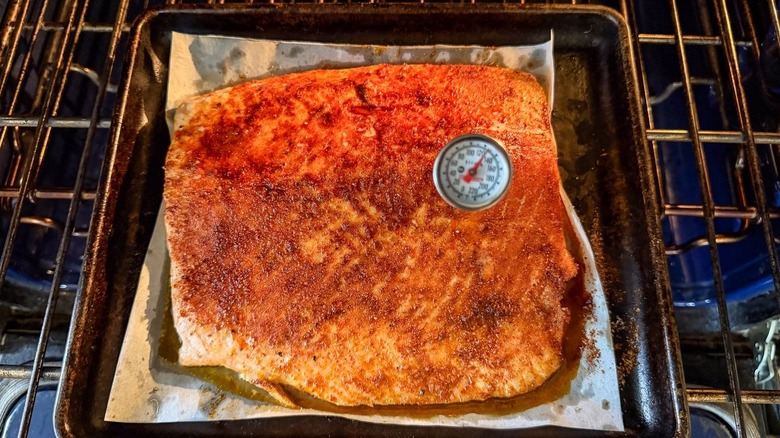 Instant read thermometer at 120 F inserted in seasoned and baked salmon filet