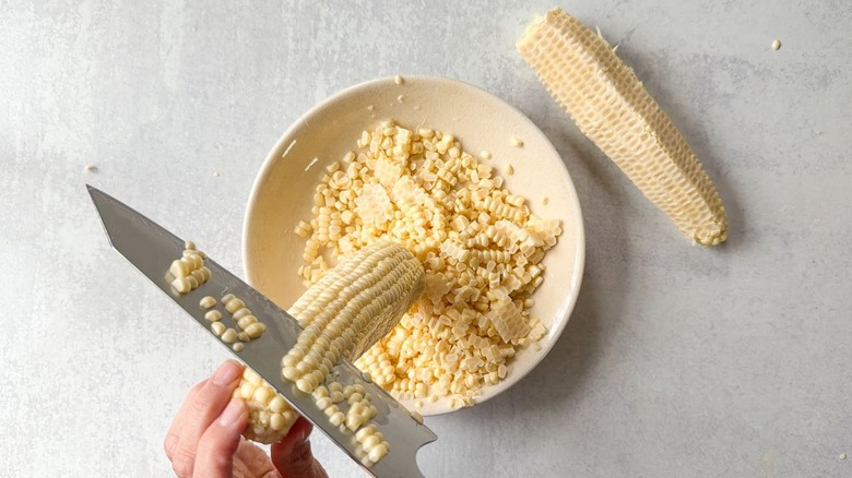 Cutting corn kernels away from cobs into a shallow bowl