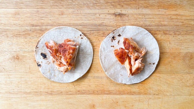 Baked and flaked salmon on white corn tortillas on cutting board